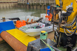 Boat being loaded onto a large yellow crane at a dock.