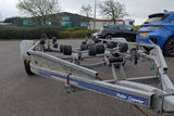 Boat trailer with wheels on a paved surface, with cars and buildings in the background.