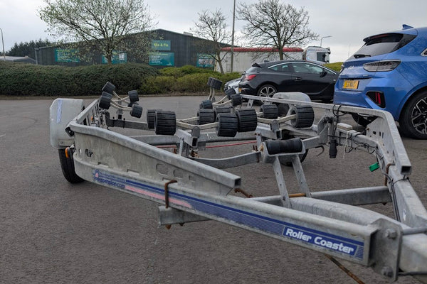 Boat trailer with wheels on a paved surface, with cars and buildings in the background.