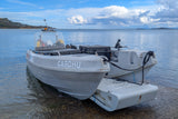 Boat with 'CARDHU' branding on a trailer at the edge of water under a cloudy sky.