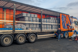 Truck with a trailer loaded with stacked items, with a person standing nearby.