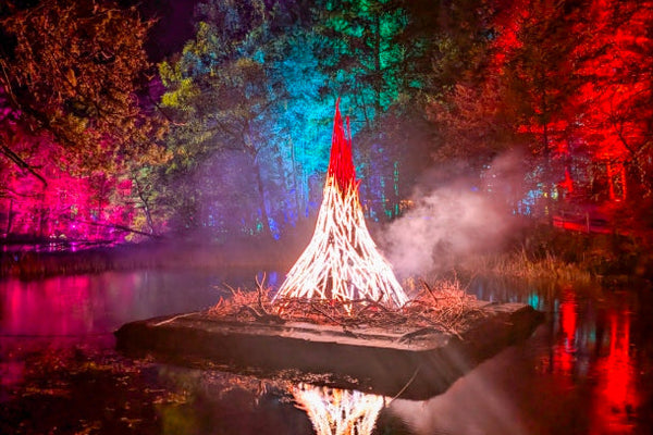 Lighted structure on a platform over water with colorful tree lights in the background