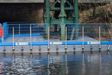Floating dock with blue safety railing in a body of water, under a bridge.